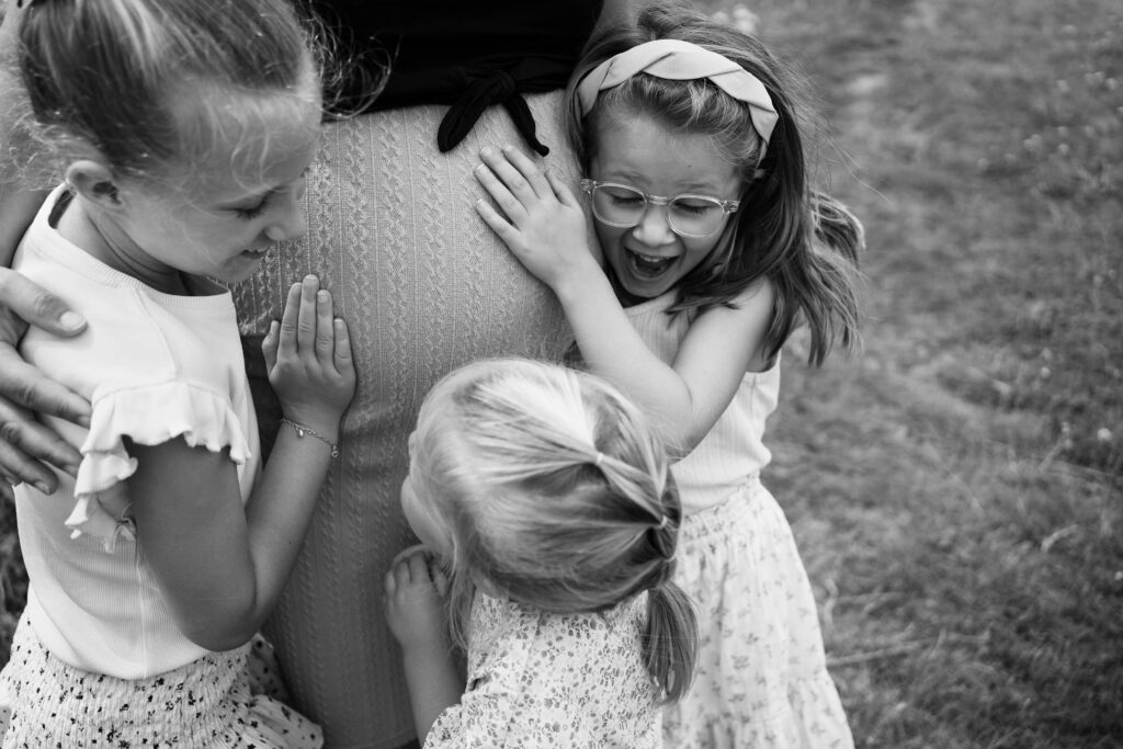 Twee kinderen lachen en knuffelen tijdens een spontane zwangerschapsfotoshoot.