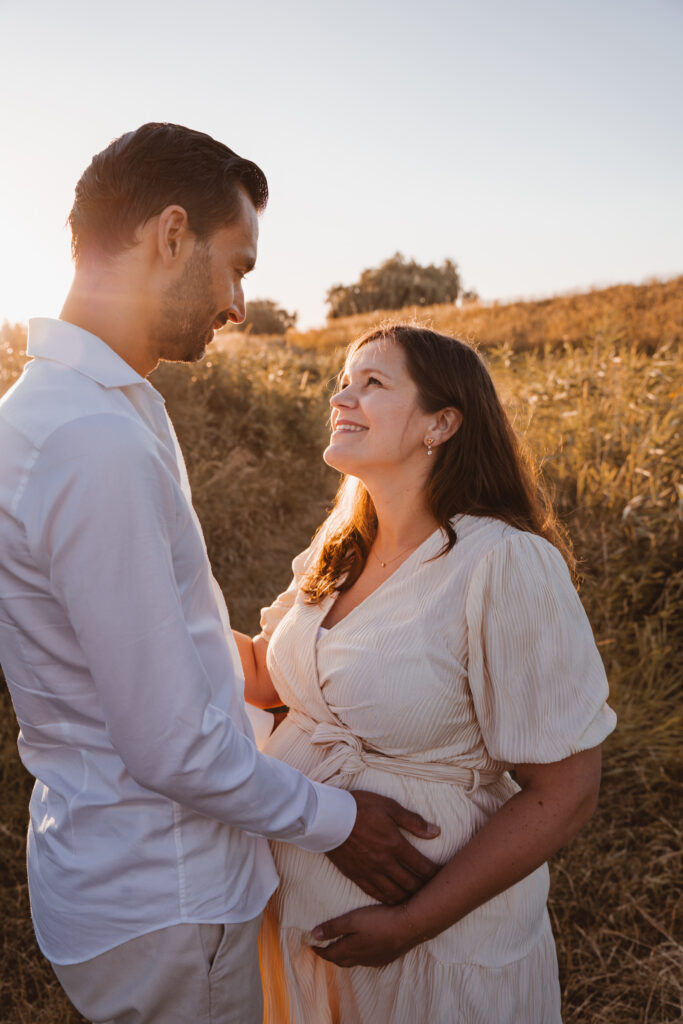 koppel wat kijkt naar elkaar tijdens zwangerschapsshoot tijdens golden hour.