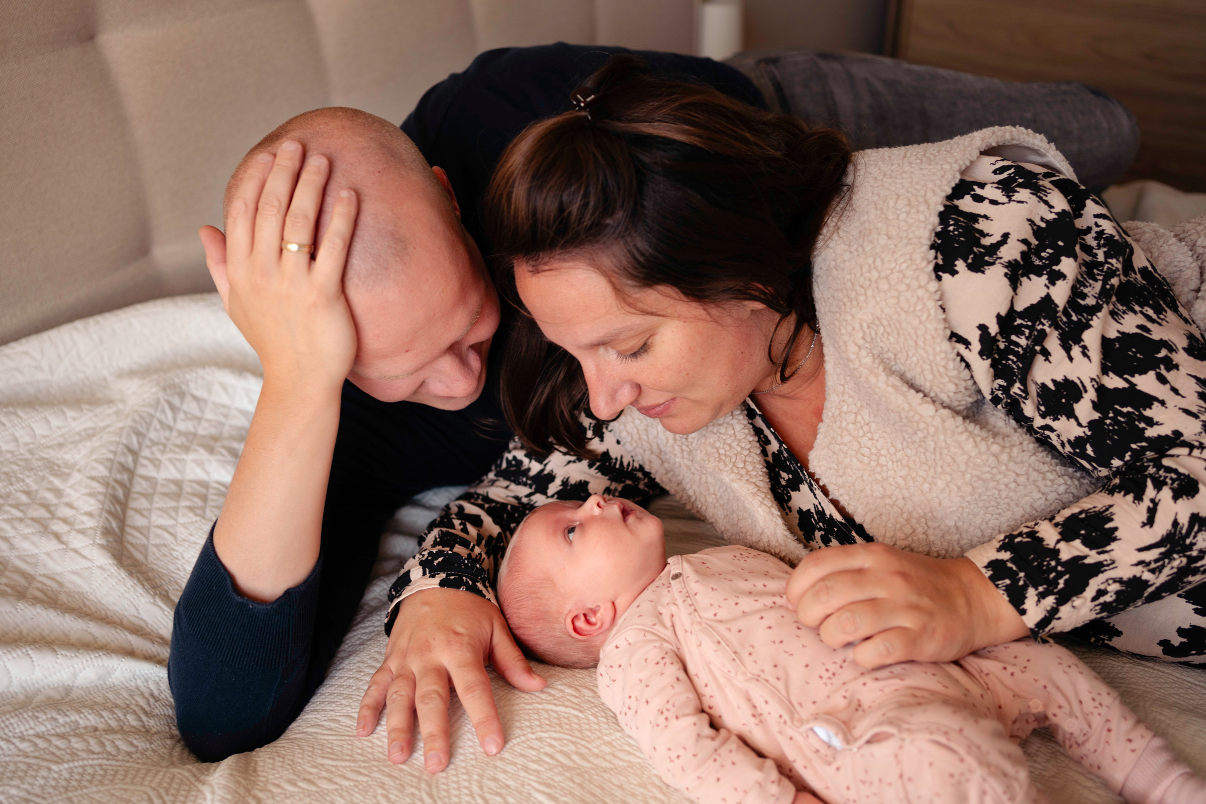 Ouders liggen op bed met de baby tijdens newbornshoot in de thuissituatie